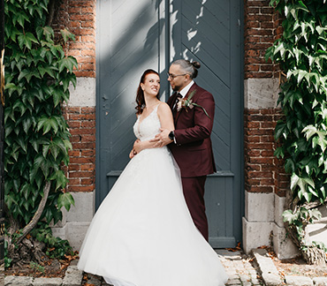 Portrait de couple de mariés en lumière naturelle le jour de leur mariage en face d'une vieille porte en bois entourée de lierre
